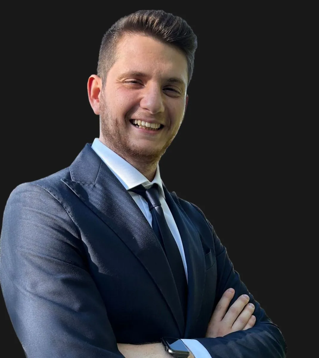 Felice Zingaro in giacca e cravatta, sorridente, a braccia conserte